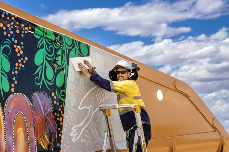 Kalsigns worker smiling and installing colourful signage on the side of a mining truck